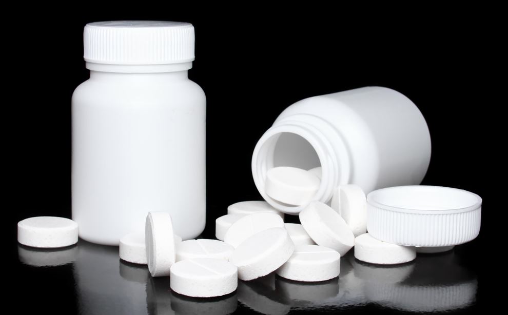 Hvide piller der ligger foran to hvide pilleglas på sort baggrund. 